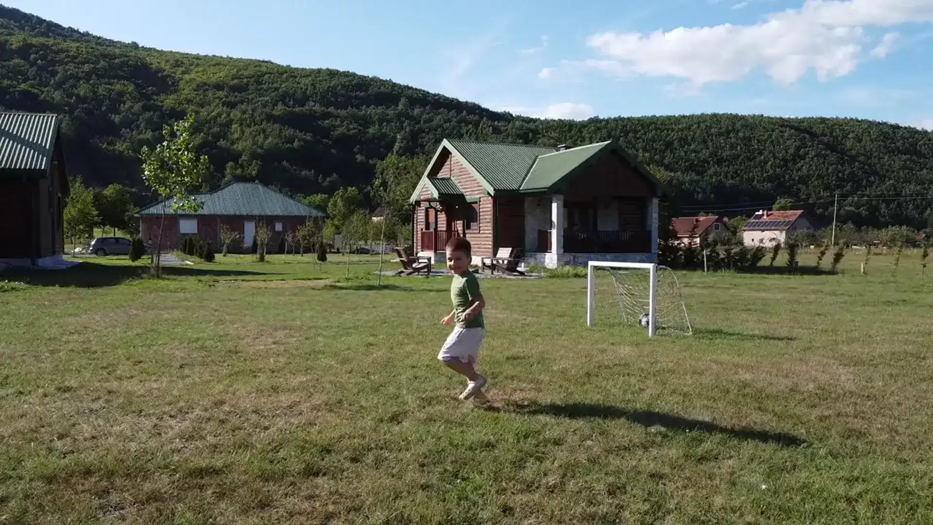 Dječak trči livadom ispred drvenih vila Eco Village-a, iza su planine
